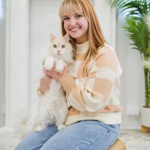Kaylee is kneeling on a rug holding a white cat